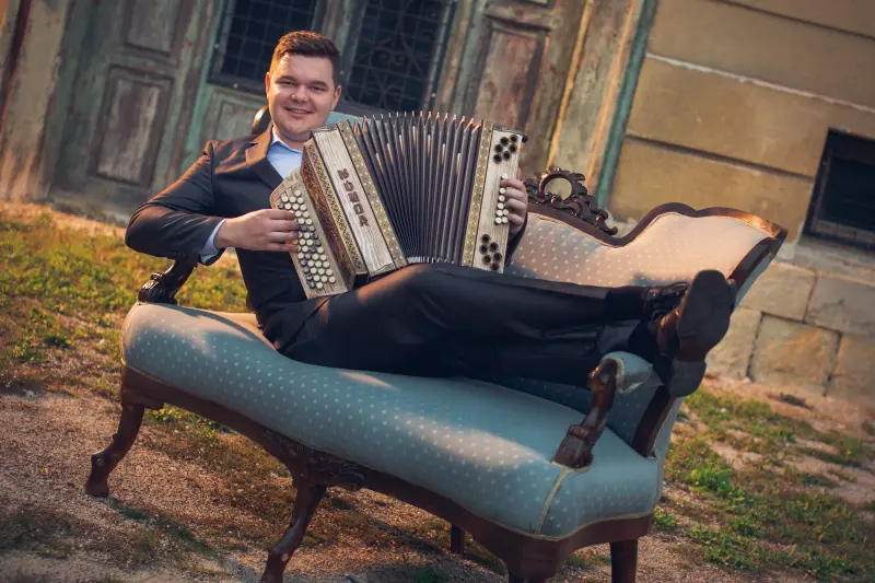 Nejc Pačnik s harmoniko Munda na zofi pred staro hišo